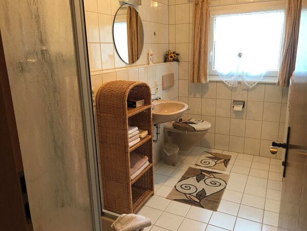 Une salle de bain équipée de toilettes, d’un lavabo, d’un panier en osier et de quelques tapis décoratifs.