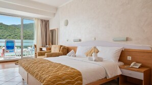 A hotel room with a bed, a bedside table with a phone, a view of a body of water, and a chair by the window. - Hotel Narcis - Maslinica Hotels and Resorts (Labin)