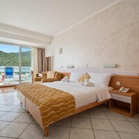 Quarto de hotel com uma cama, mesa de cabeceira com telefone, vista para um corpo d'água e uma cadeira junto à janela.