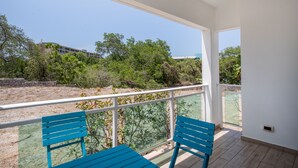 A balcony with two blue chairs, a white railing, and a view of greenery and buildings. - Electricity Included in rental price! (Willemstad)
