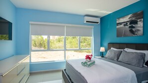 A bedroom with a bed, a desk, a chair, a window, and a wall-mounted air conditioner. - Electricity Included in rental price! (Willemstad)