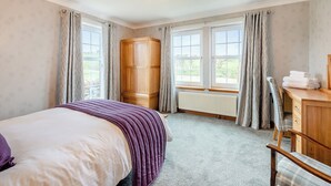 A bedroom with a bed, a wooden wardrobe, a radiator, and a window with curtains. - 4 bedroom accommodation in Kingarth (Kingarth)