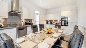 A modern kitchen with white cabinets, a built-in oven, and a dining area with a long table set for six. - 4 bedroom accommodation in Kingarth (Kingarth)