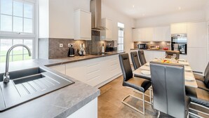 A modern kitchen with a large island, built-in appliances, and a dining area with chairs. - 4 bedroom accommodation in Kingarth (Kingarth)