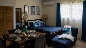Habitación de hotel con cama, una mesa de comedor con sillas, una mesita con tazas y un florero, y un sillón con una manta.