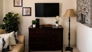 Una sala de estar con un mueble de madera oscura, un sofá color beige, una planta grande en maceta, una lámpara de pie y un televisor de pantalla plana montado en la pared.