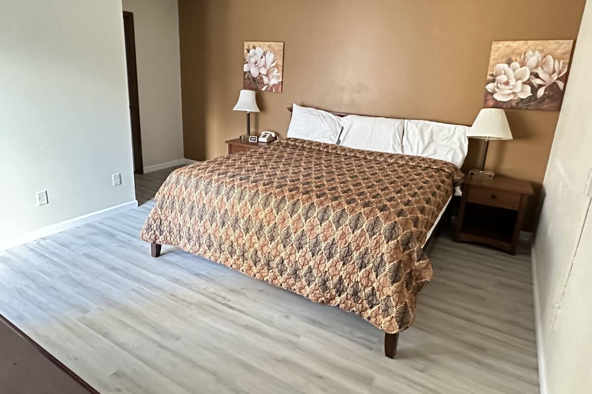A bedroom with a large bed, two bedside tables with lamps, and floral artwork on the walls.