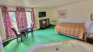 Hotelkamer met een bed, bureau, stoel, televisie, een klein tafeltje en een badkamer met bad.