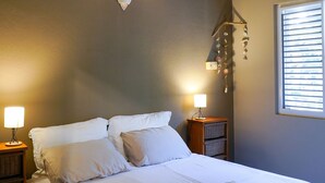 Een slaapkamer met een bed, bedlampen, een wandairconditioner, een decoratie en een raam met zonwering.