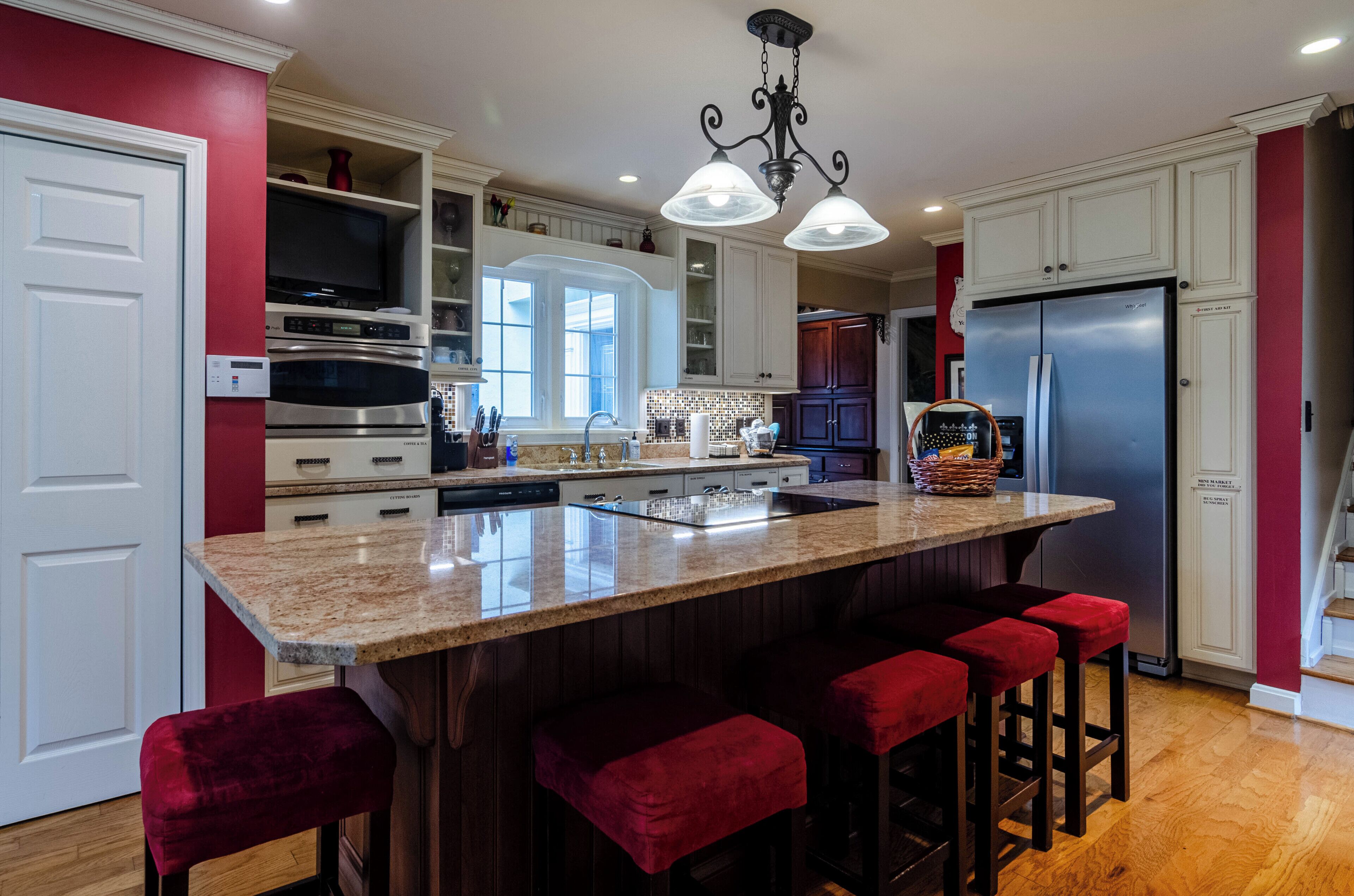 A modern kitchen with a large island, bar stools, stainless steel appliances, and a red accent wall.