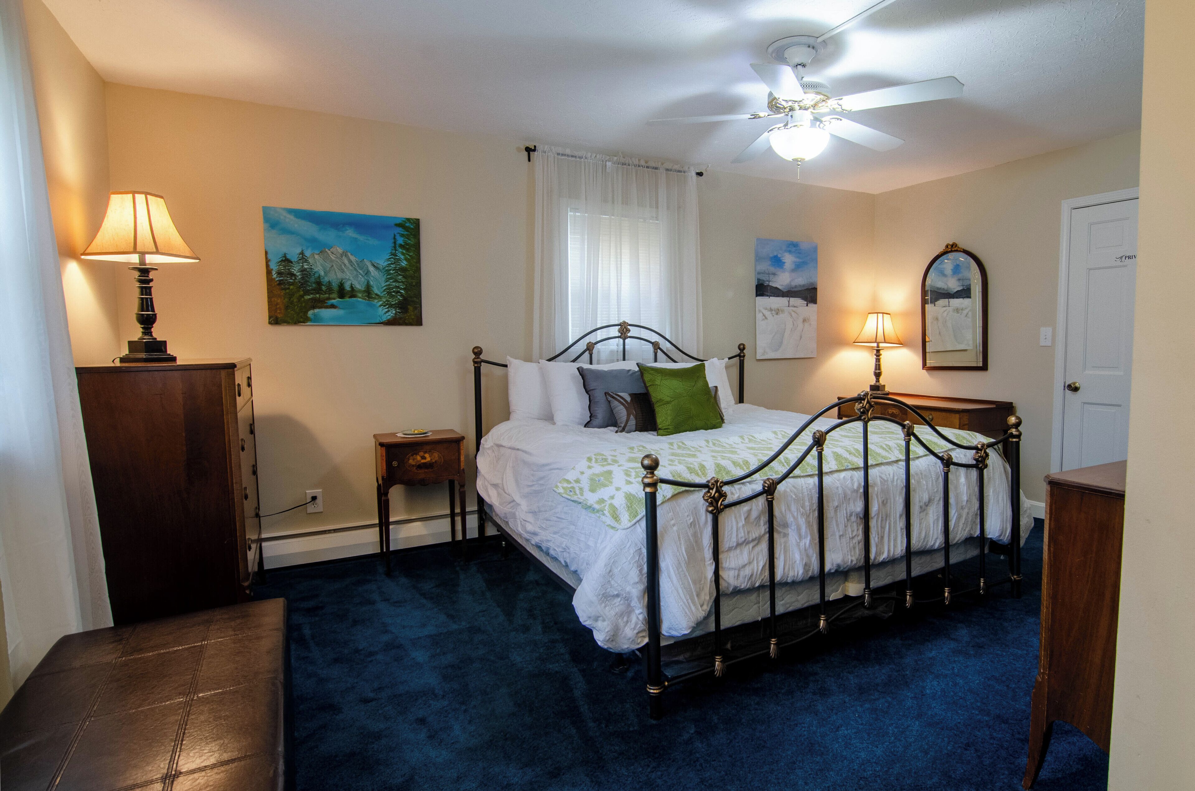 A bedroom with a bed, two bedside tables, a ceiling fan, and artwork on the walls.