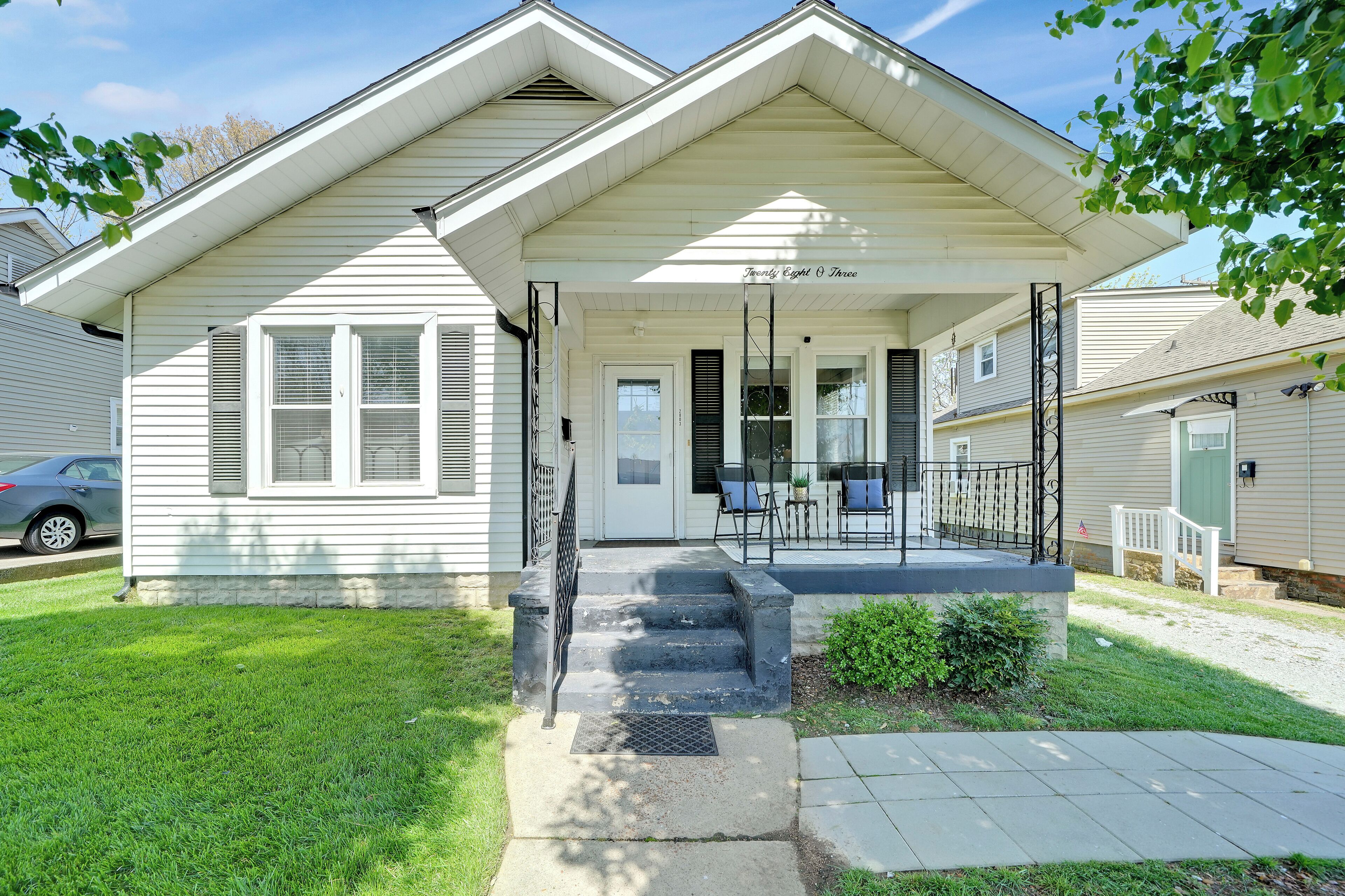 A two-story house with a front porch, a small front yard, and a visible garage.