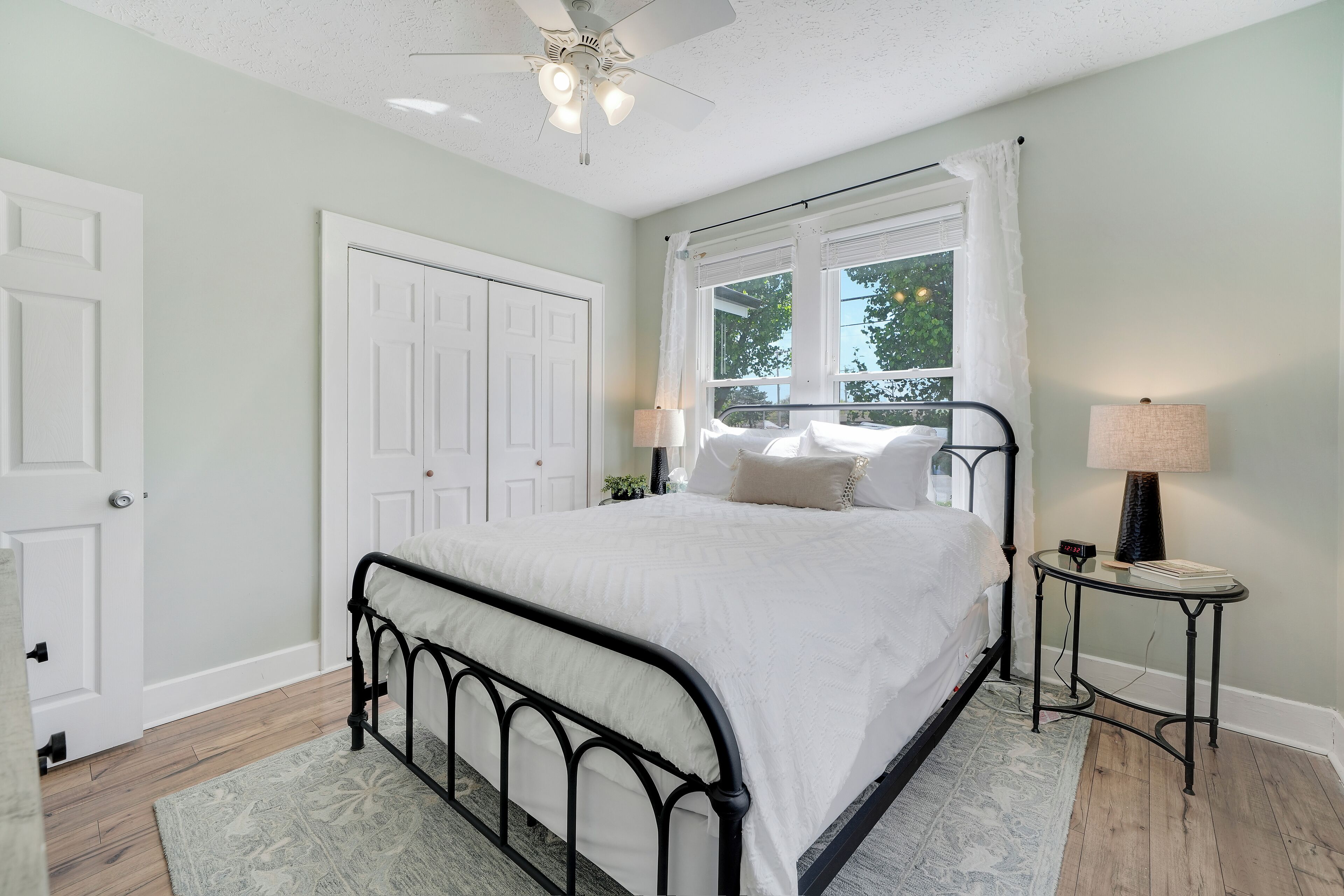 A bedroom with a bed, a nightstand, a ceiling fan, and a window with curtains.