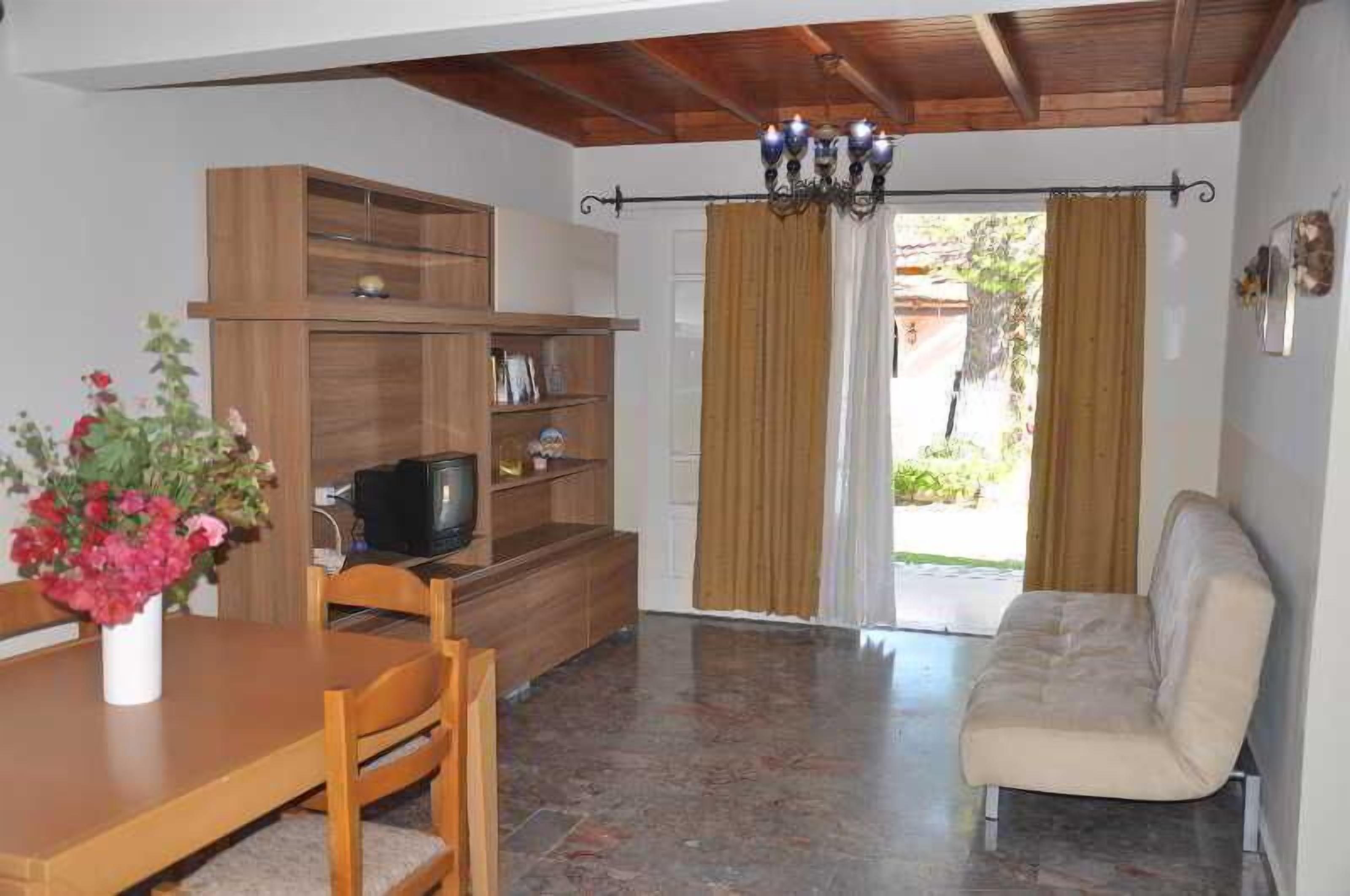 A living room with a wooden TV stand, a sofa, a dining table with chairs, and a chandelier.