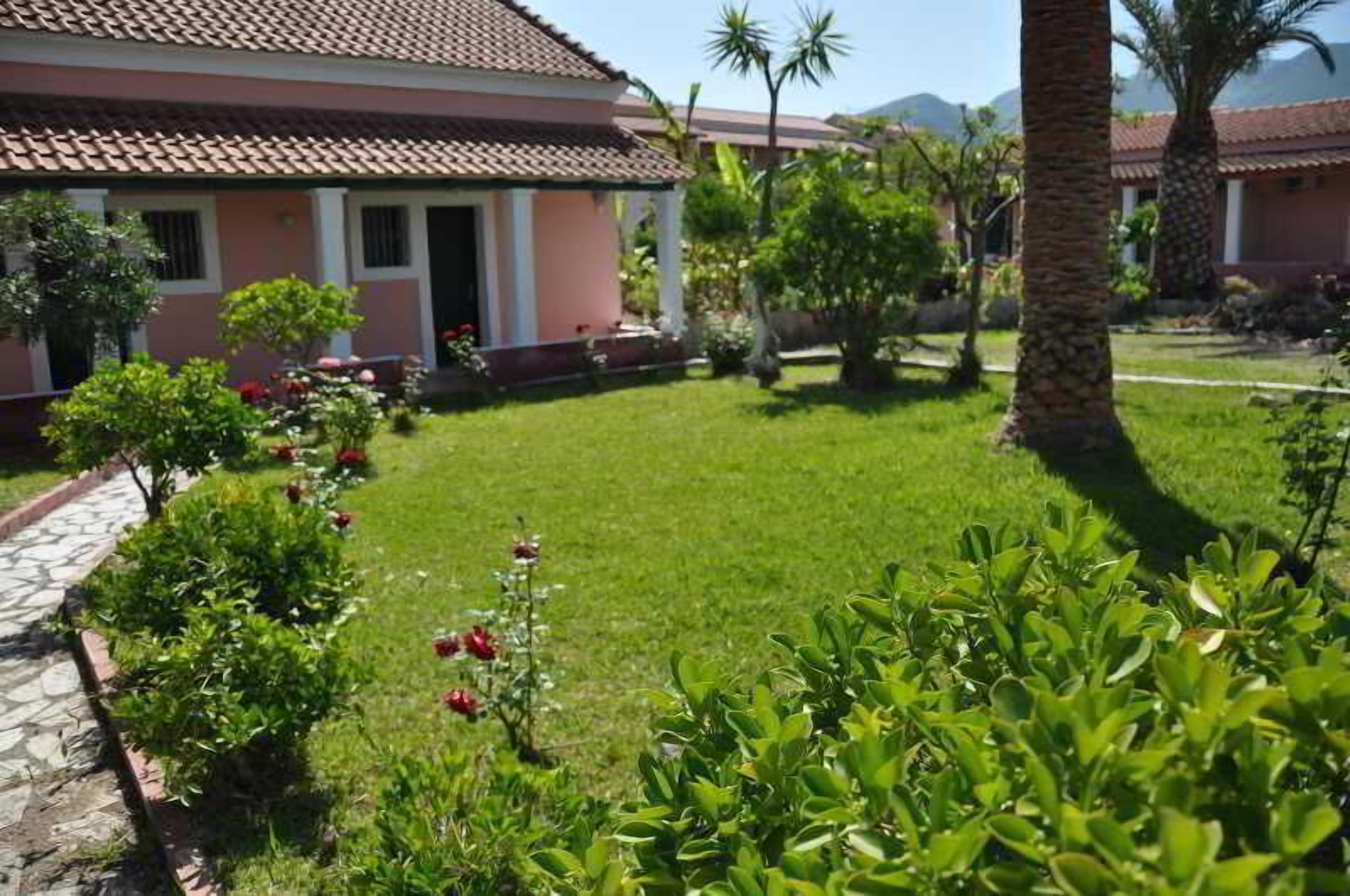 A house with a tiled roof, a well-maintained lawn, and various plants.
