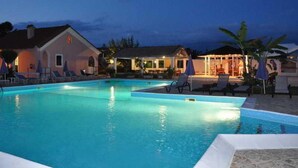 A swimming pool with lounge chairs and umbrellas, surrounded by buildings with outdoor seating areas. - Tassos Apartments (Corfu)