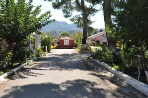 A paved pathway leading to a red building surrounded by greenery and trees. - Tassos Apartments (Corfu)