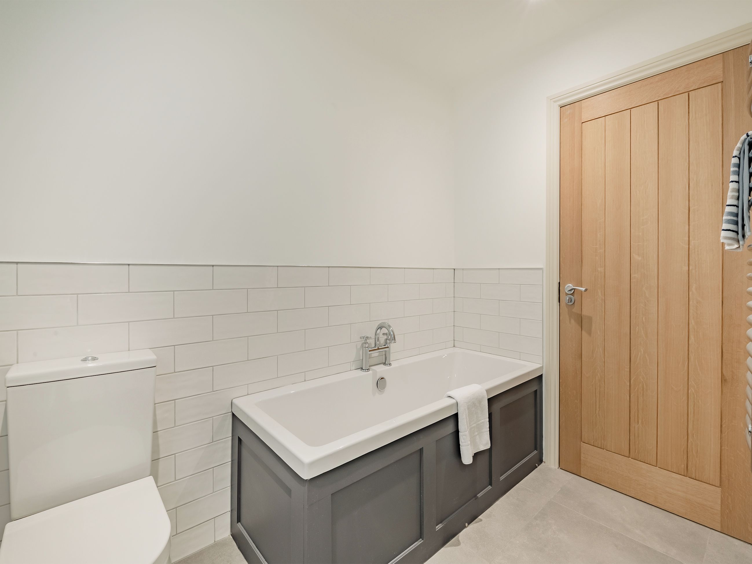 A bathroom with a white toilet, a white sink with a towel, and a wooden door.