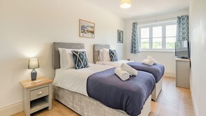 A double bed with a headboard, bedside tables, a lamp, a television, and a window with curtains.