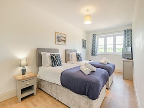A double bed with a headboard, bedside tables, a lamp, a television, and a window with curtains.