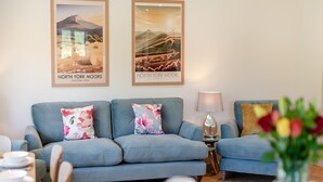 A living room with a blue sofa set, two framed posters of North York Moors, a lamp, and a vase with flowers. - 3 bedroom accommodation in Ruswarp, near Whitby (Ruswarp, near Whitby)