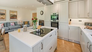 A modern kitchen with white cabinetry, a built-in oven, and a central island with a kettle.