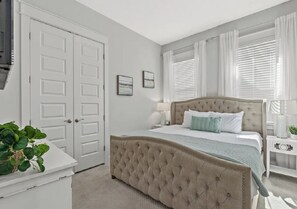 A bedroom with a tufted headboard bed, white walls, and a door with a handle.