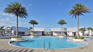 Un área de piscina con sillas de descanso y palmeras, rodeada de edificios con techos metálicos.