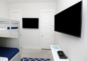 A room with bunk beds, a desk with a computer, a flat-screen TV, and a door.