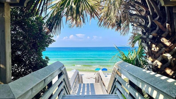 Una escalera de madera que lleva a una playa con agua turquesa cristalina y palmeras.