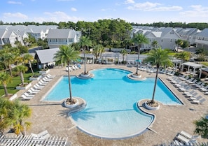 A resort with a central swimming pool surrounded by lounge chairs and palm trees.