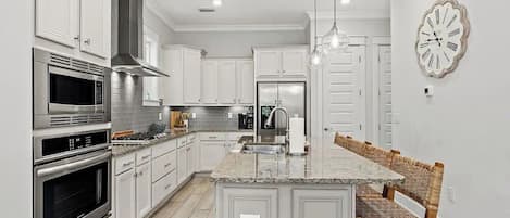 Una cocina moderna con armarios blancos, electrodomésticos de acero inoxidable, una isla central con asientos y un reloj de pared.
