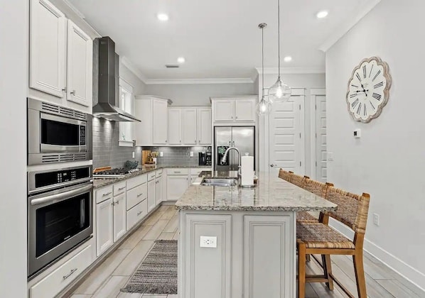 A modern kitchen with white cabinetry, stainless steel appliances, a central island with seating, and a wall clock.