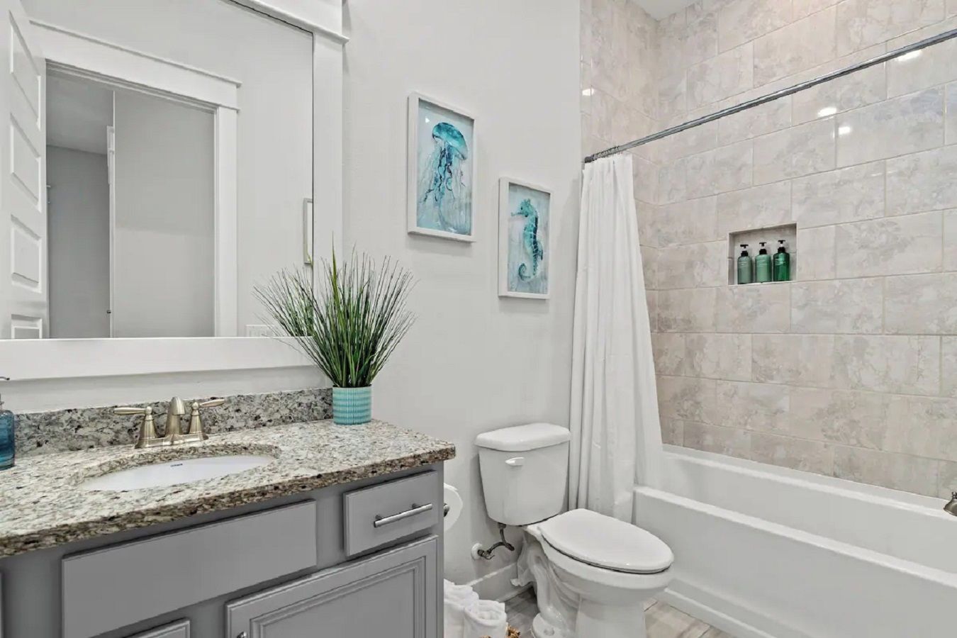 Une salle de bain avec un comptoir en granit, des toilettes, une douche avec un rideau et une étagère murale contenant des articles de toilette.