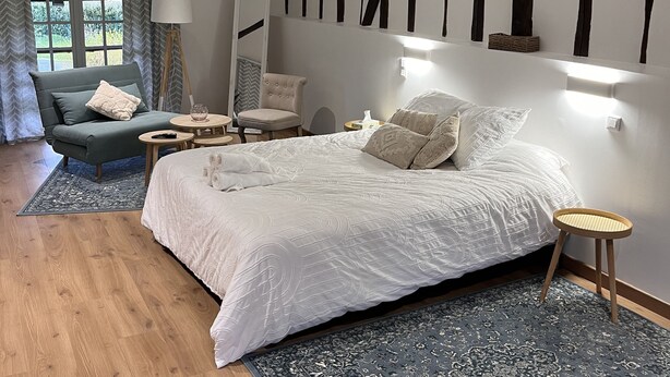 Une chambre à coucher avec un grand lit, une chaise, une petite table et une lampe.