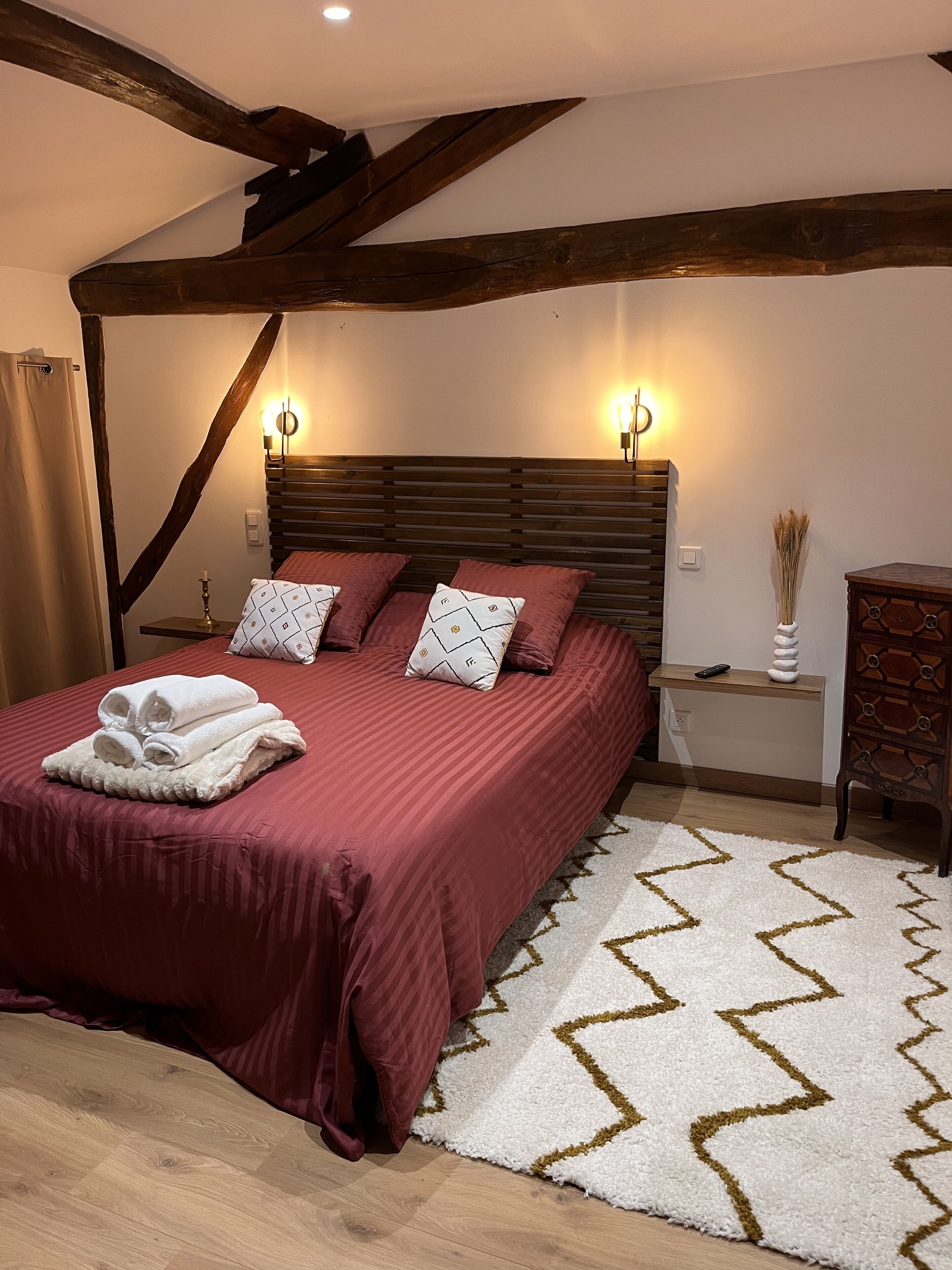 A bedroom with a wooden headboard, a red bedspread, and a white rug with a geometric pattern.