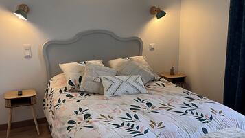 Een net opgemaakt bed met een deken met bloemenprint, twee bedlampjes en een wandlamp.