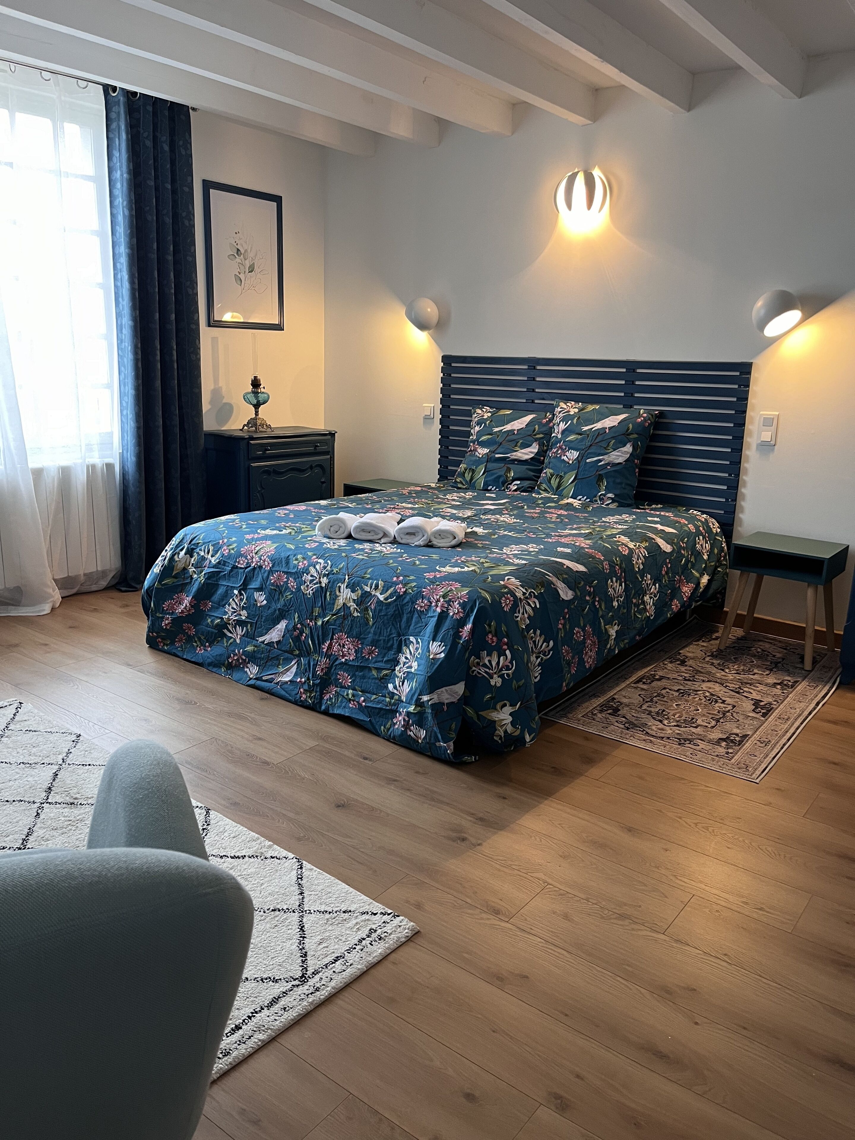 A bedroom with a bed, bedside tables, a nightstand, a lamp, a chair, and a rug.