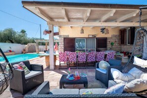 An outdoor patio area with a pool, seating arrangements, and a covered section with a table and chairs. - Villa Sunflower Alghero (ALGHERO)