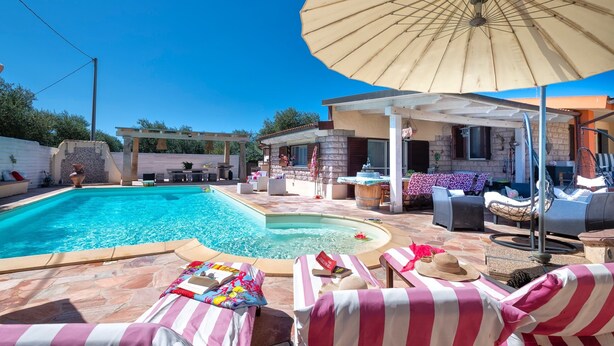 A backyard with a swimming pool, lounge chairs, and a covered patio area.