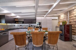 A modern kitchen with a dining area, featuring a central island, built-in appliances, and a stone accent wall. - Villa Sunflower Alghero (ALGHERO)