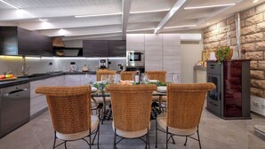 A modern kitchen with a dining area, featuring a central island, stainless steel appliances, and wicker chairs.