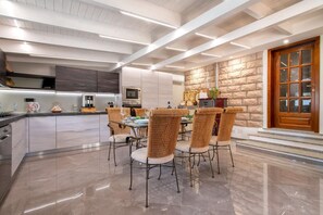 A modern kitchen with a central island, dining area with wicker chairs, and a stone accent wall. - Villa Sunflower Alghero (ALGHERO)