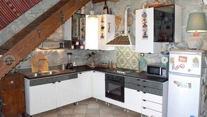 Une cuisine avec des armoires blanches, une cuisinière, un four à micro-ondes et un réfrigérateur. Le plafond est en bois et un des murs est en pierre.