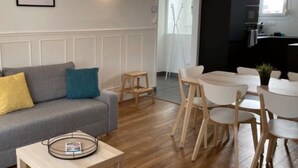 Ein modernes Wohnzimmer mit einem grauen Sofa, einem kleinen Couchtisch und einem Essbereich mit einem weißen Tisch und Holzstühlen.