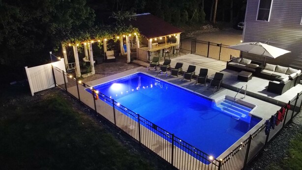 A swimming pool with a surrounding deck, a covered seating area, and a pergola with string lights.