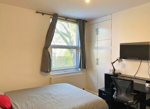 A bedroom with a bed, a desk with a chair, a television, and a wardrobe.