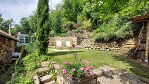 Un giardino con muri in pietra, una scala in pietra, un pergolato in legno e un muro in pietra con una porta in legno.