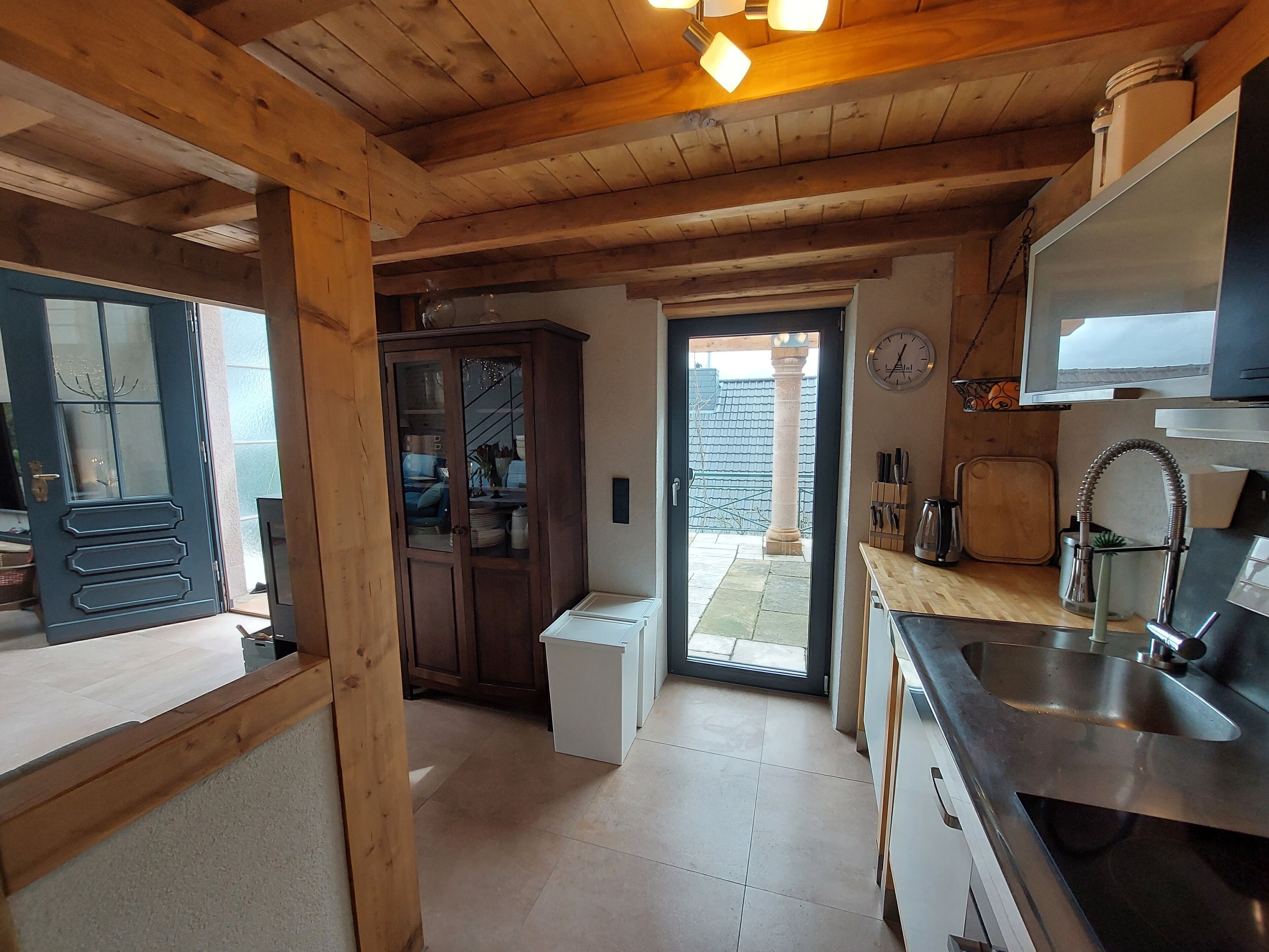 A kitchen with wooden beams, a built-in cabinet, a sink, and a clock on the wall.