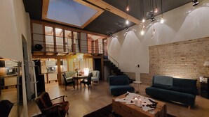 Un'ampia zona giorno con soffitto alto, una scala e una cucina sullo sfondo.